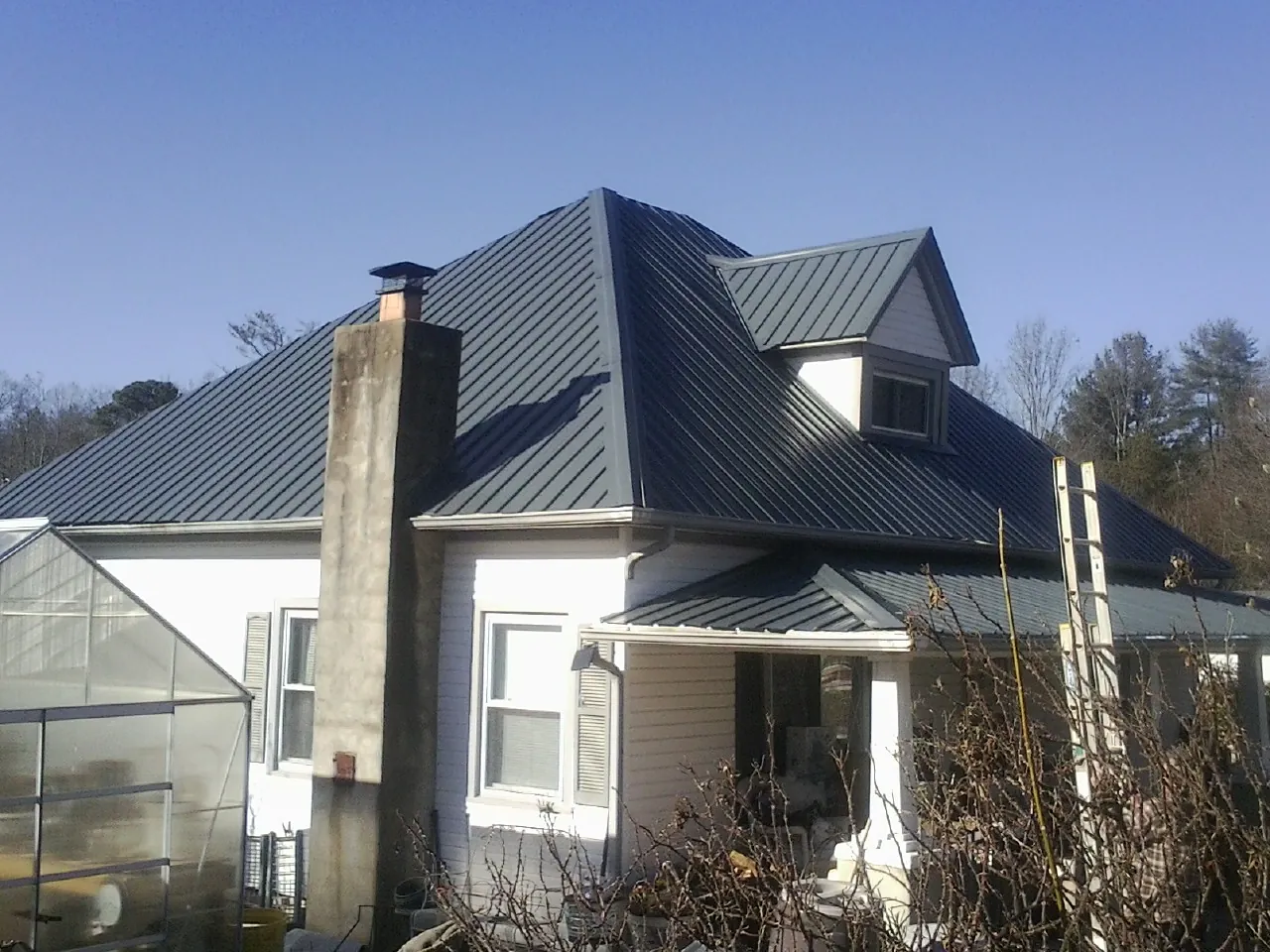 Dark blue standing seam metal roof on a white farmhouse with dormer — Slate & Tile Roof Repair by Roofing Brothers in Goodfield