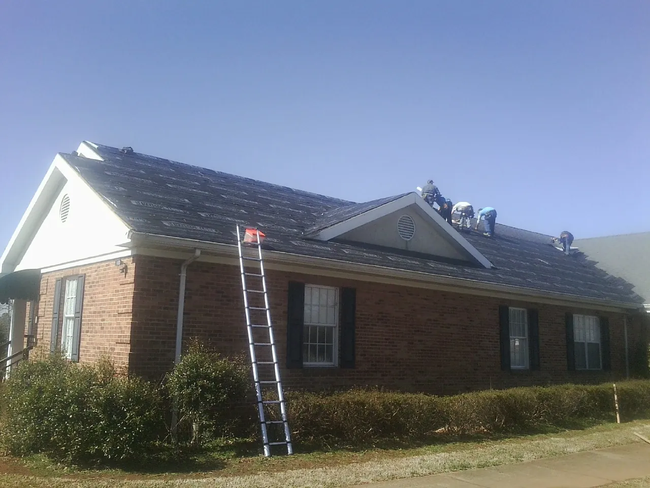 Crew tearing shingles off a brick ranch roof with a ladder set — Metal Roof Repair work by our crew in Goodfield