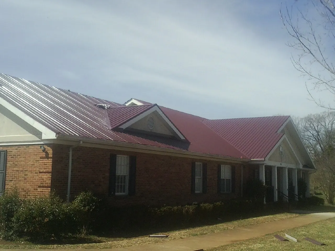 Red metal roof with gabled entries on a long brick building, from a Hail Damage Roof Repair job in Goodfield