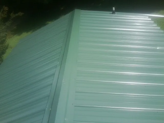 New green metal panels meeting at the ridge of a roof — Flat Roof Repair work by our crew in Goodfield