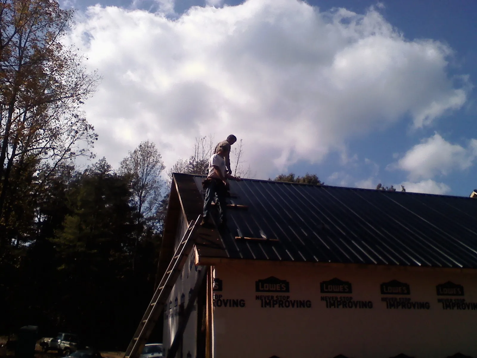 Roofer fastening dark metal panels high against a cloudy sky, from a Roof Inspection job in Goodfield